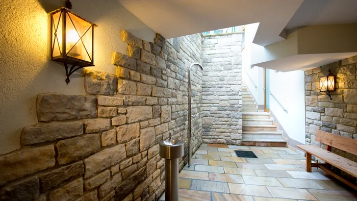 Wellnessbereich mit Steinfliesen, Wandlampen, Edelstahldusche und Treppe nach oben
